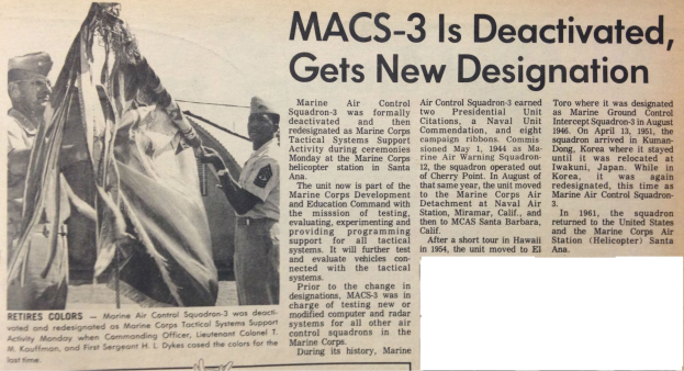 Zeitungstitel 'Macs-3 ist deaktiviert, erhält neue Bezeichnung' mit einer Gruppe von uniformierten Menschen, die ein Tuch halten, lächeln und feierlich wirken, vor einem hellblauen Himmel mit weißen Wolken, mit fetter schwarzer Schrift.