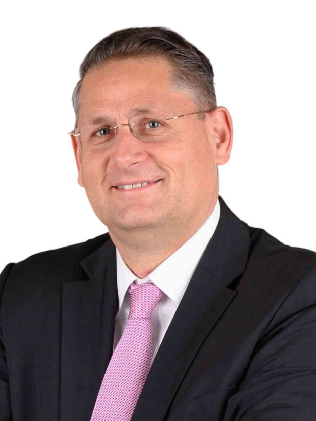 Ein Mann im Anzug und mit Krawatte, der eine Brille trägt, lächelt in die Kamera vor einem weißen Hintergrund, was darauf hindeutet, dass er ein Finanzberater ist.