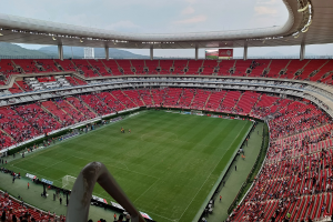 Ein großes Stadion voller Zuschauer bei einem Fußballspiel, mit Hügeln und einem klaren blauen Himmel im Hintergrund.