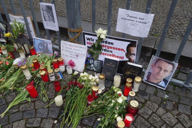 Gedenkstätte in Berlin mit Blumen, Kerzen, Fotos und Plakaten vor einem Zaun.