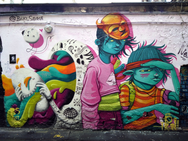 Mural auf einem Gebäude mit Graffiti, das eine Straße am Boden, Strommasten und einen klaren blauen Himmel im Hintergrund zeigt.