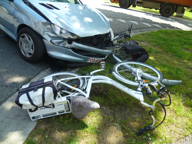 Auto am Straßenrand mit einem Fahrrad in der Nähe liegend, Bäume und klarer blauer Himmel im Hintergrund.