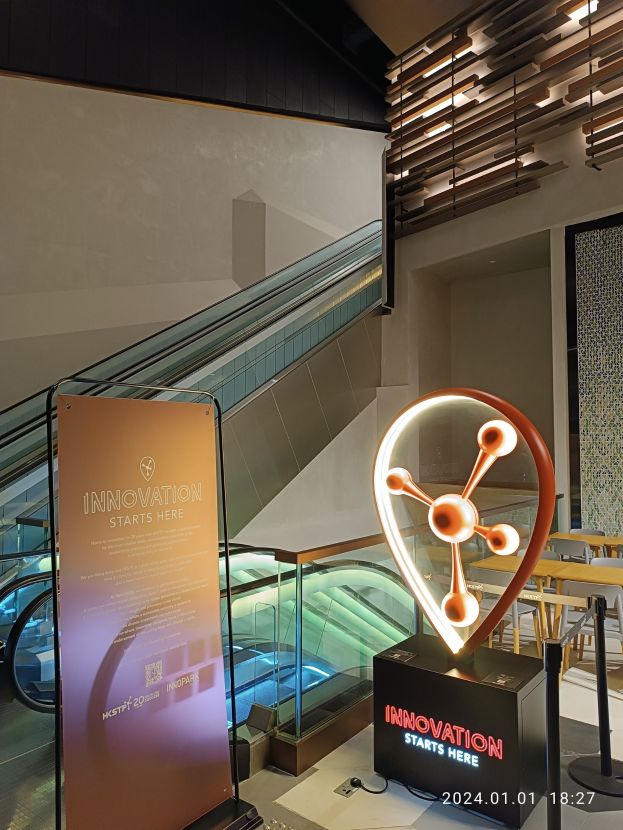 Große Tafel in einem Geböude mit einer Rolltreppe im Hintergrund, Tische und Stühle auf der rechten Seite und eine Tafel mit "Innovation Starts Here" auf der linken Seite, was auf die HSTP20 Expo hinweist.