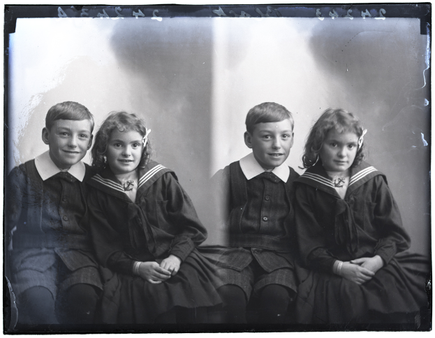 Vier Kinder in Schuluniform, zwei Jungen und zwei Mädchen, die fröhlich in einem Schwarz-Weiß-Foto posieren.