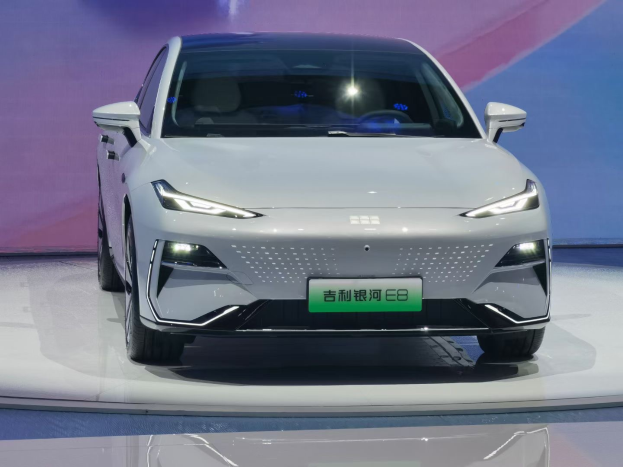 Ein weißer Elektrowagen mit eleganten Linien und einem glänzenden Finish wird auf einer Automesse präsentiert, im Hintergrund steht eine Tafel mit der Aufschrift "E8 Elektroauto in China gestartet".