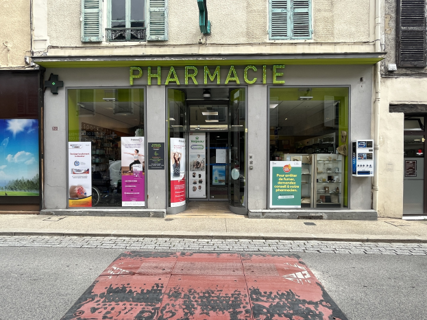 Apotheke mit Glaswänden und -türen, Plakate an den Wänden, an einer Straßenecke gelegen.