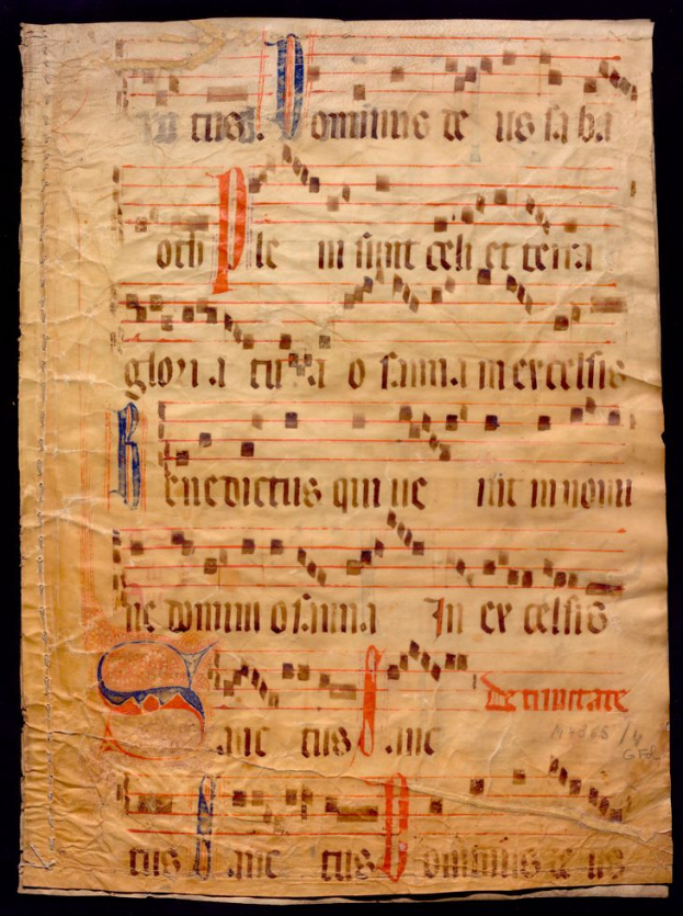 Ein illuminiertes Manuskript mit Musiknotation auf einem Stück Papier vor einem dunklen Hintergrund, gefüllt mit Text und Musiksymbolen, die ein komplexes Design bilden.