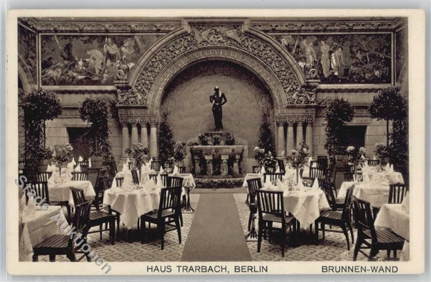 Schwarzes und weißes Foto eines alten Berliner Restaurantinnenraums mit Tischen, Stühlen, Blumenvasen, einer Statue, Wandskulpturen, Pflanzen und Text unten.