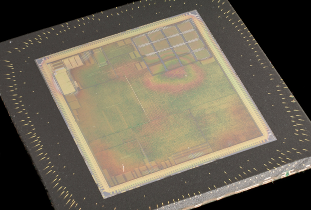 Nahaufnahme eines rechteckigen Halbleiterchips mit metallischem Glanz, schmalem Metallrahmen und kleinen L├Âchern an den Kanten auf schwarzem Hintergrund mit leicht erh├Âhten R├Ąndern.